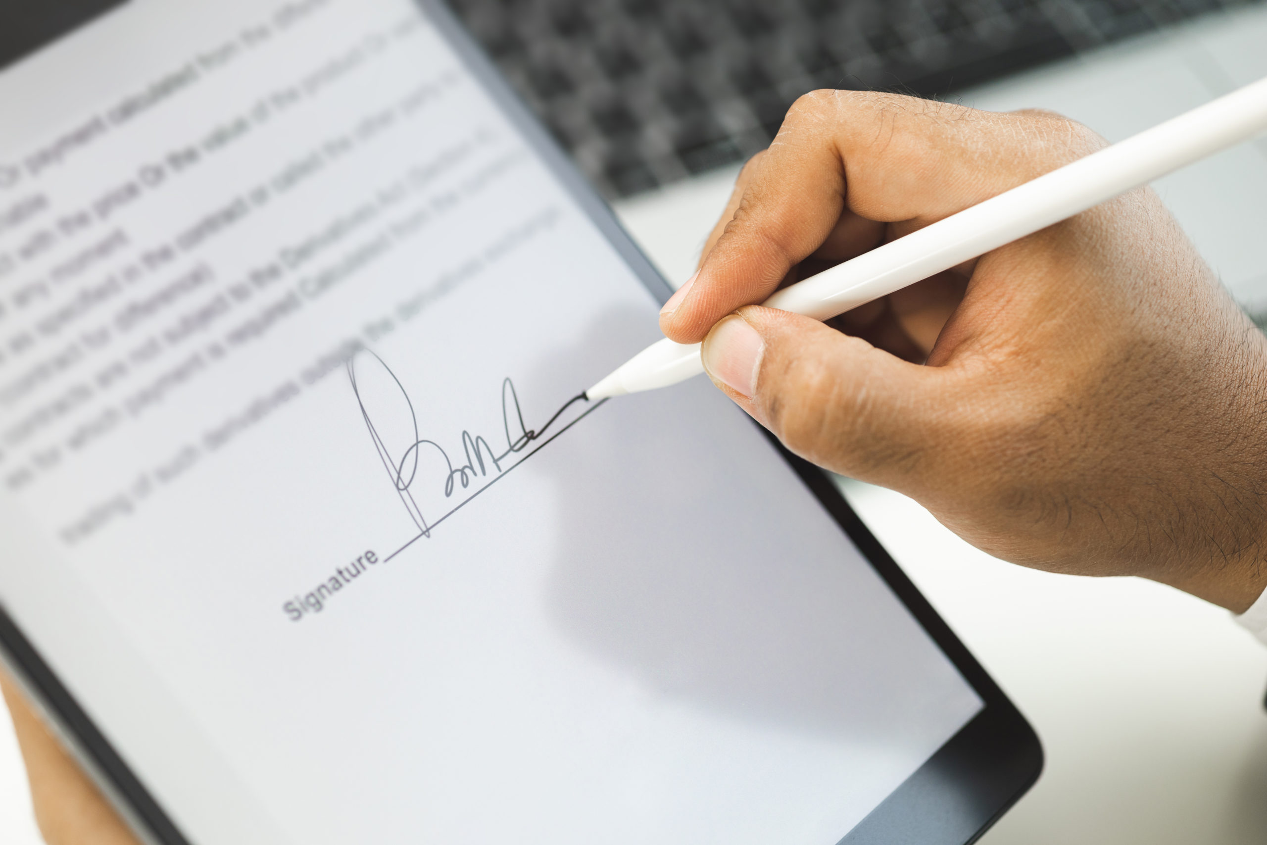 Elektronische Signaturen. docu-fix.de. Hand eines Manns unterschreibt mit einem digitalen Stift auf einem Tablet einen Vertrag